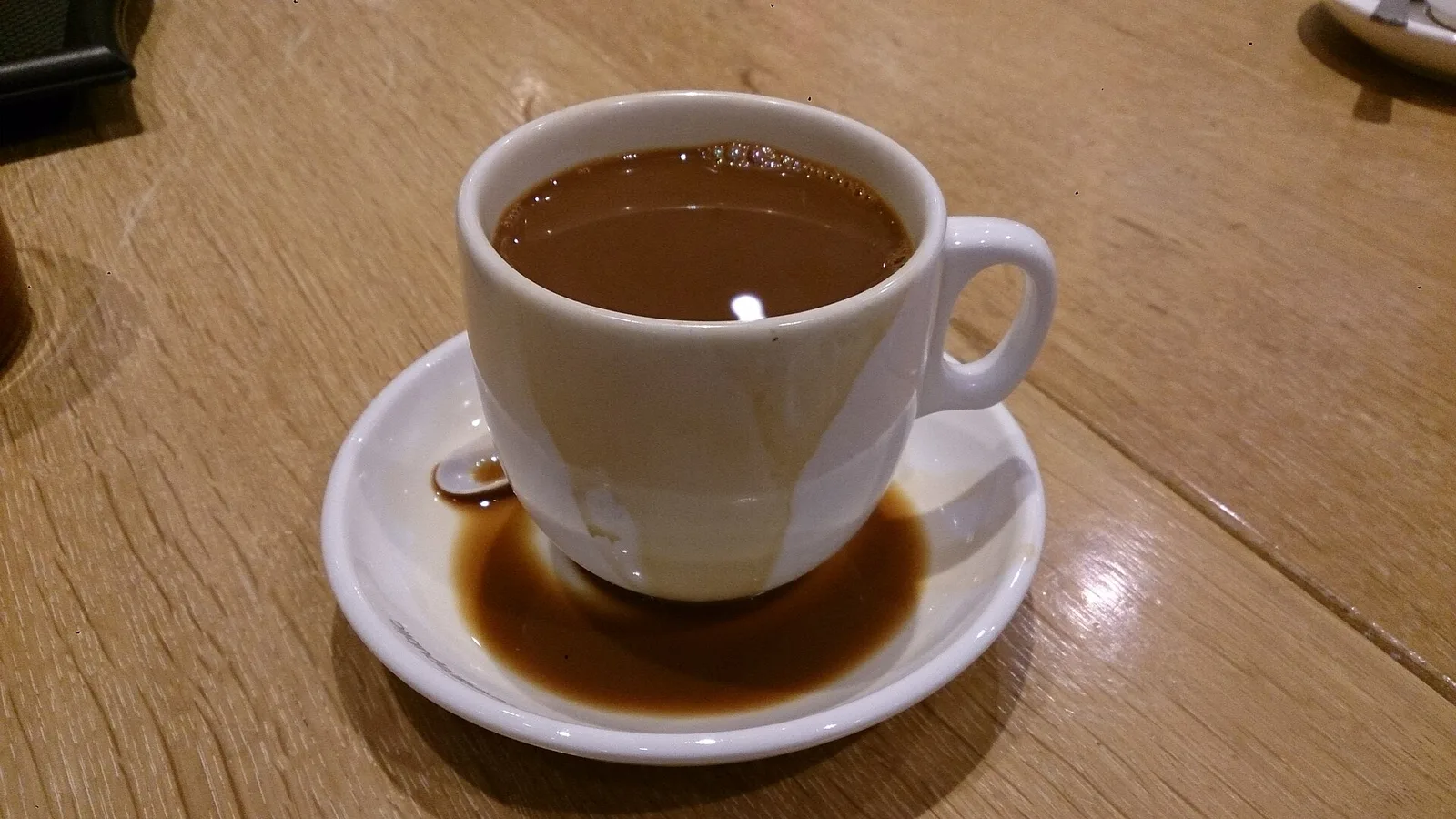 A cup of coffee with milk on a saucer on a wooden cafe table.