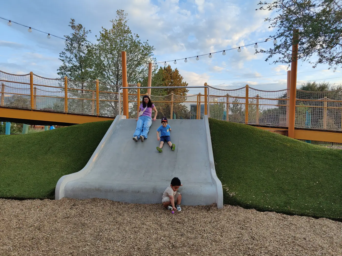 Children slide down a hillside slide at the Camden Park playground.