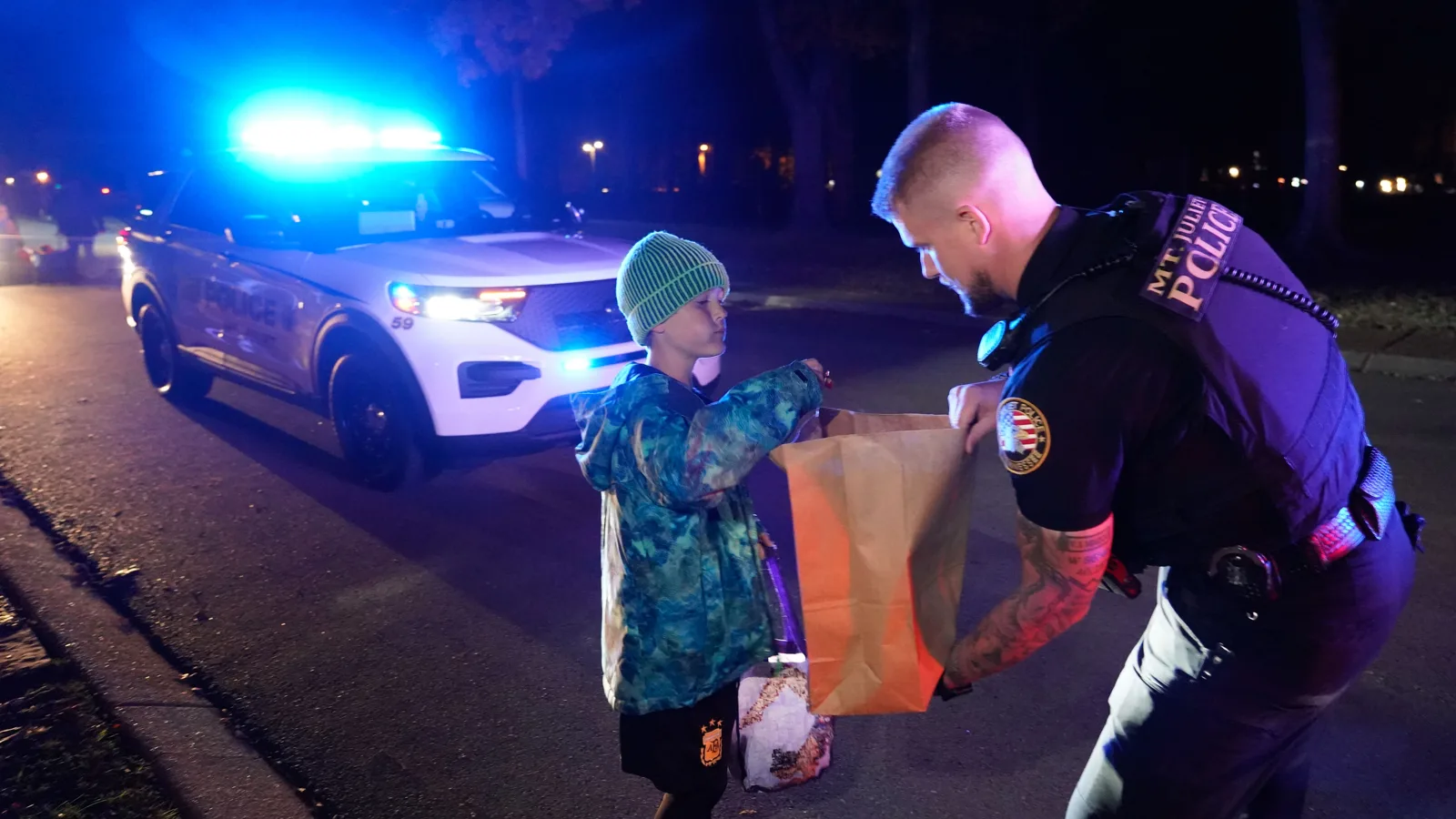 A Mt. Juliet police officer hands a bag of candy to a trick-or-treater beside a patrol car.