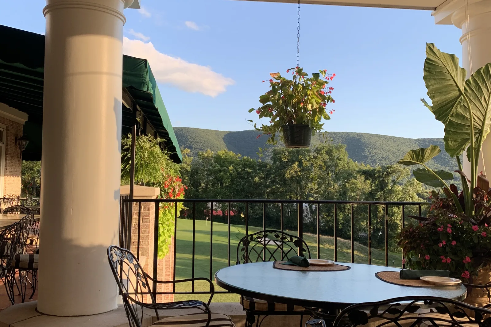 Tables on a covered restaurant patio overlooking a golf course and wooded hills.