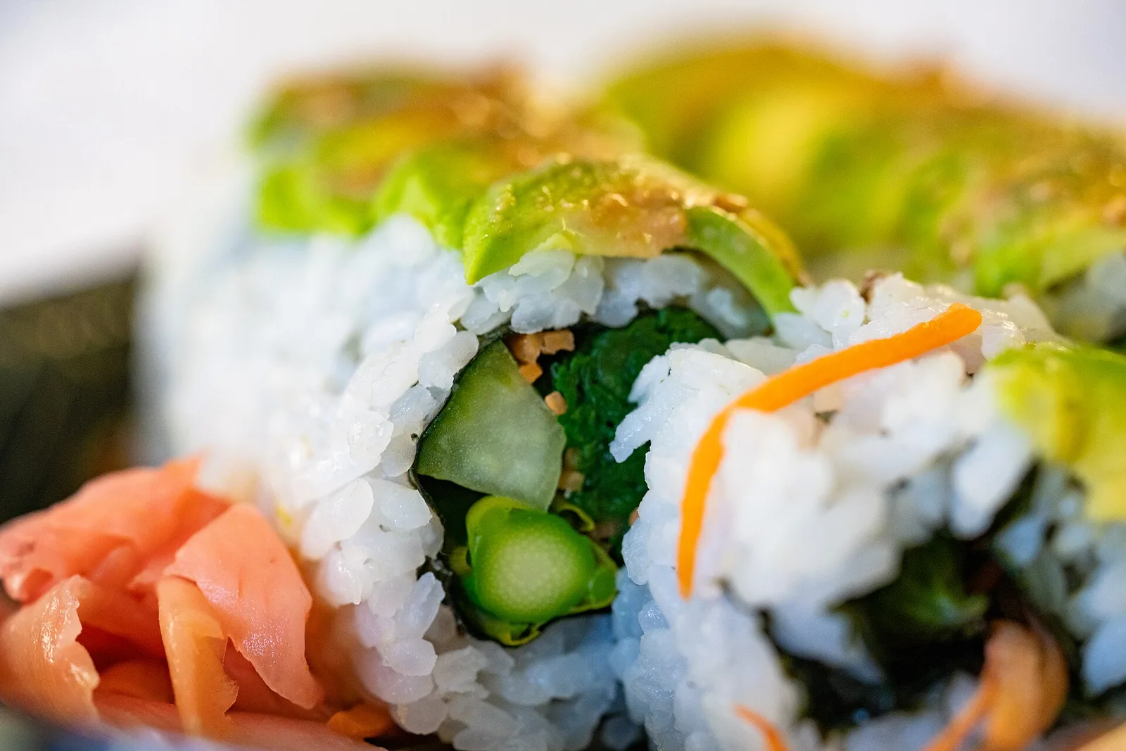 Vegetable sushi rolls topped with avocado, with pickled ginger on the side.