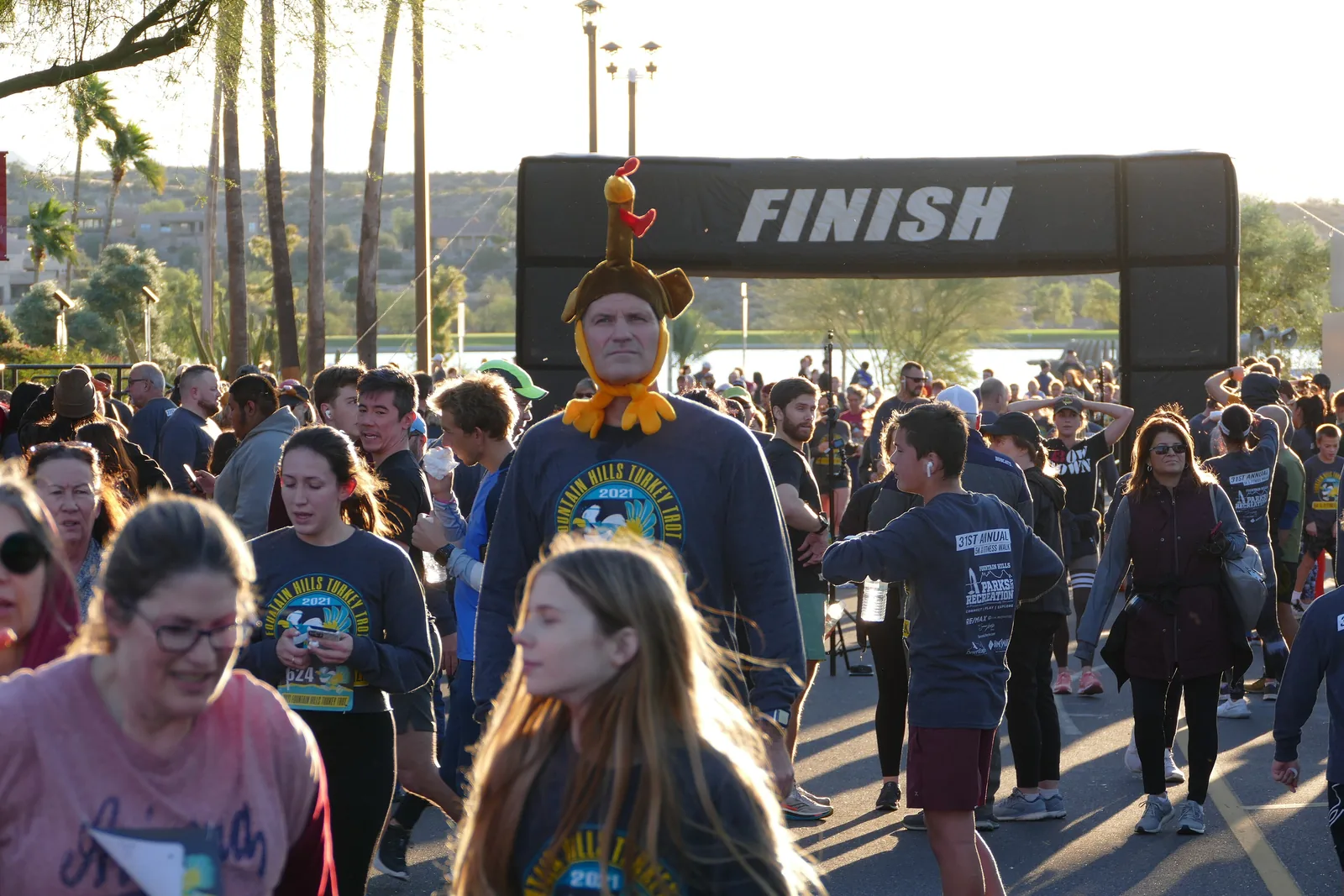 A runner in a turkey hat walks past the finish line among finishers of the Fountain Hills Turkey Trot in Fountain Hills, Ariz.