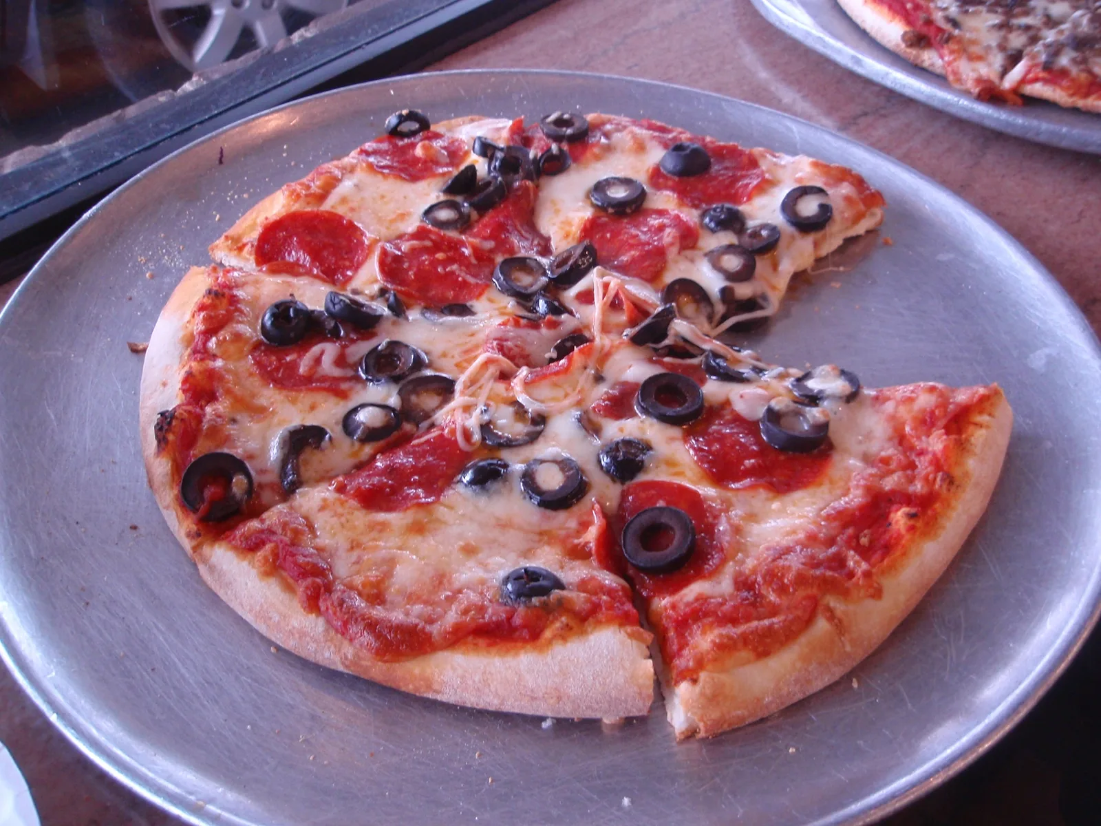 A pepperoni and black olive pizza on a metal serving tray.